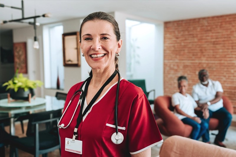 A smiling healthcare professional wearing crimson scrubs and wearing a stethoscope around her neck