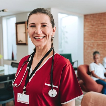 A smiling healthcare professional wearing crimson scrubs and wearing a stethoscope around her neck