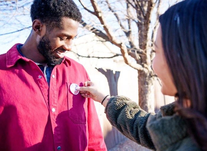 A woman places an "I voted" sticker on a man's shirt