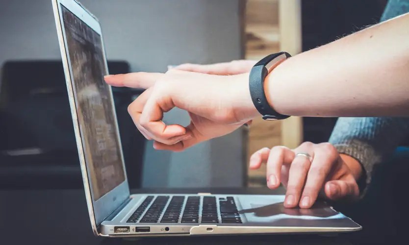 Hands typing on a laptop keyboard and pointing at the screen