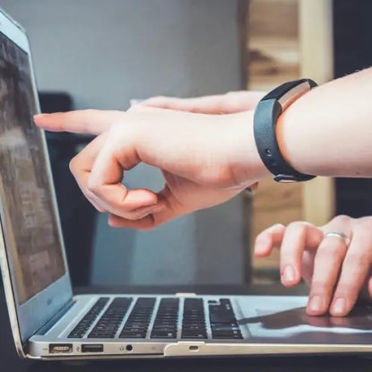 Hands typing on a laptop keyboard and pointing at the screen