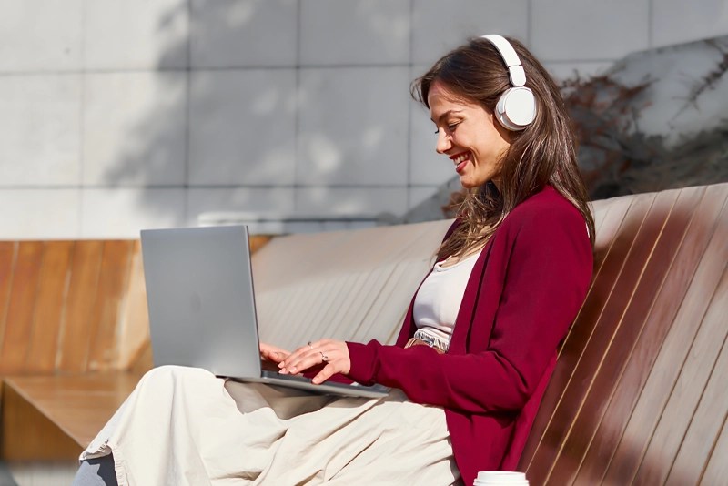 A woman wearing headphones smiles as she types on her laptop computer