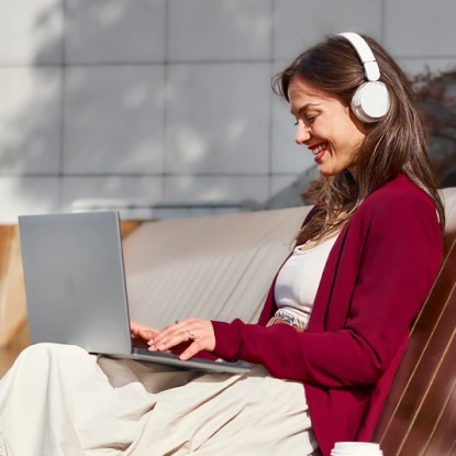 A woman wearing headphones smiles as she types on her laptop computer