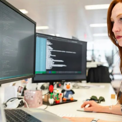 A woman working at a desk with two large computer monitors