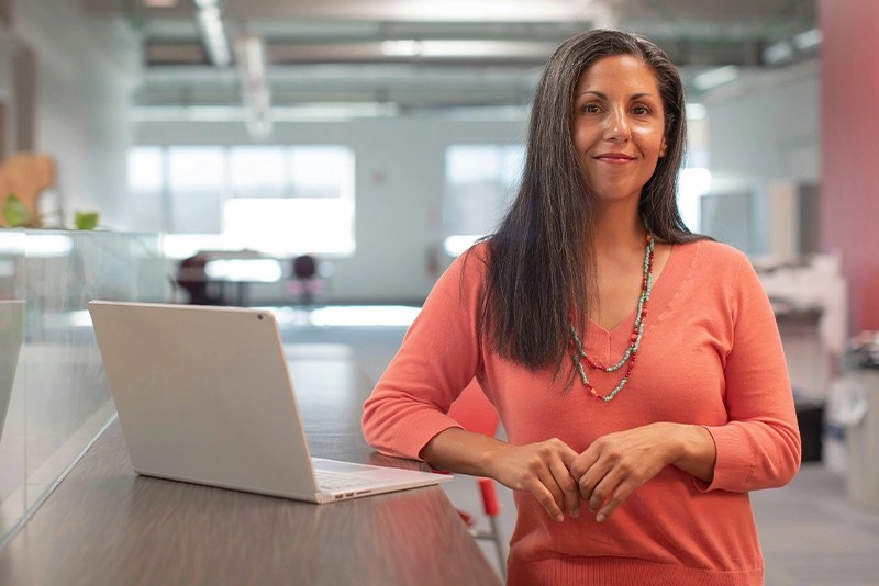 A woman posing next to a laptop computer in an office setting