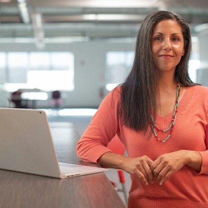 A woman posing next to a laptop computer in an office setting