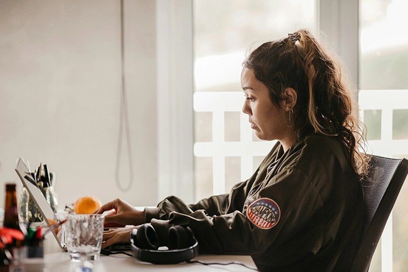 A woman in a military jacket typing on a laptop computer keyboard