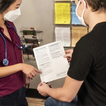 A medical staffer wearing a mask assists a patient