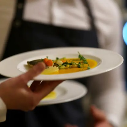 A restaurant server's hand holding a colorful dinner dish