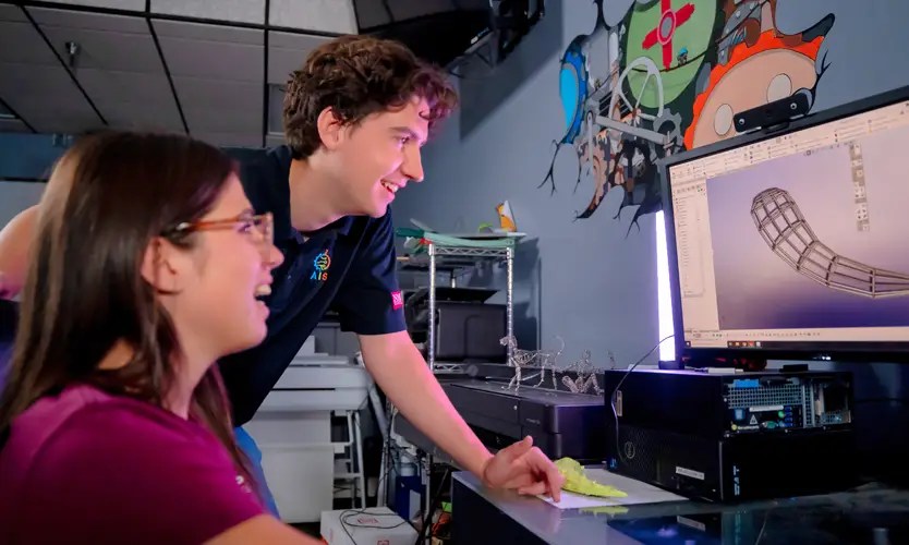 Two engineering students smiling as they look at a computer monitor