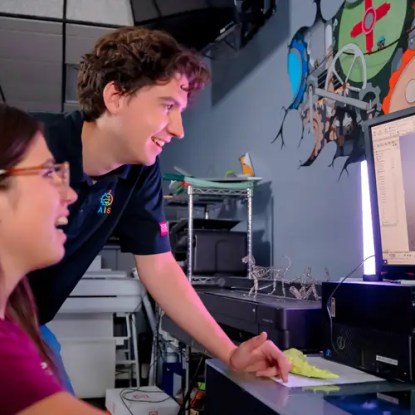 Two engineering students smiling as they look at a computer monitor