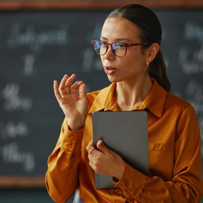 A bilingual Spanish-speaking professional stands in front of a classroom representing online degrees at NMSU Global Campus