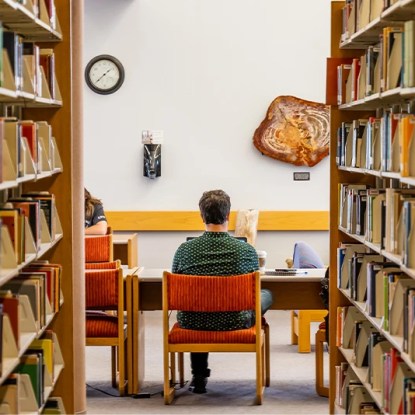 College students studying at a table between bookshelves in a university library.